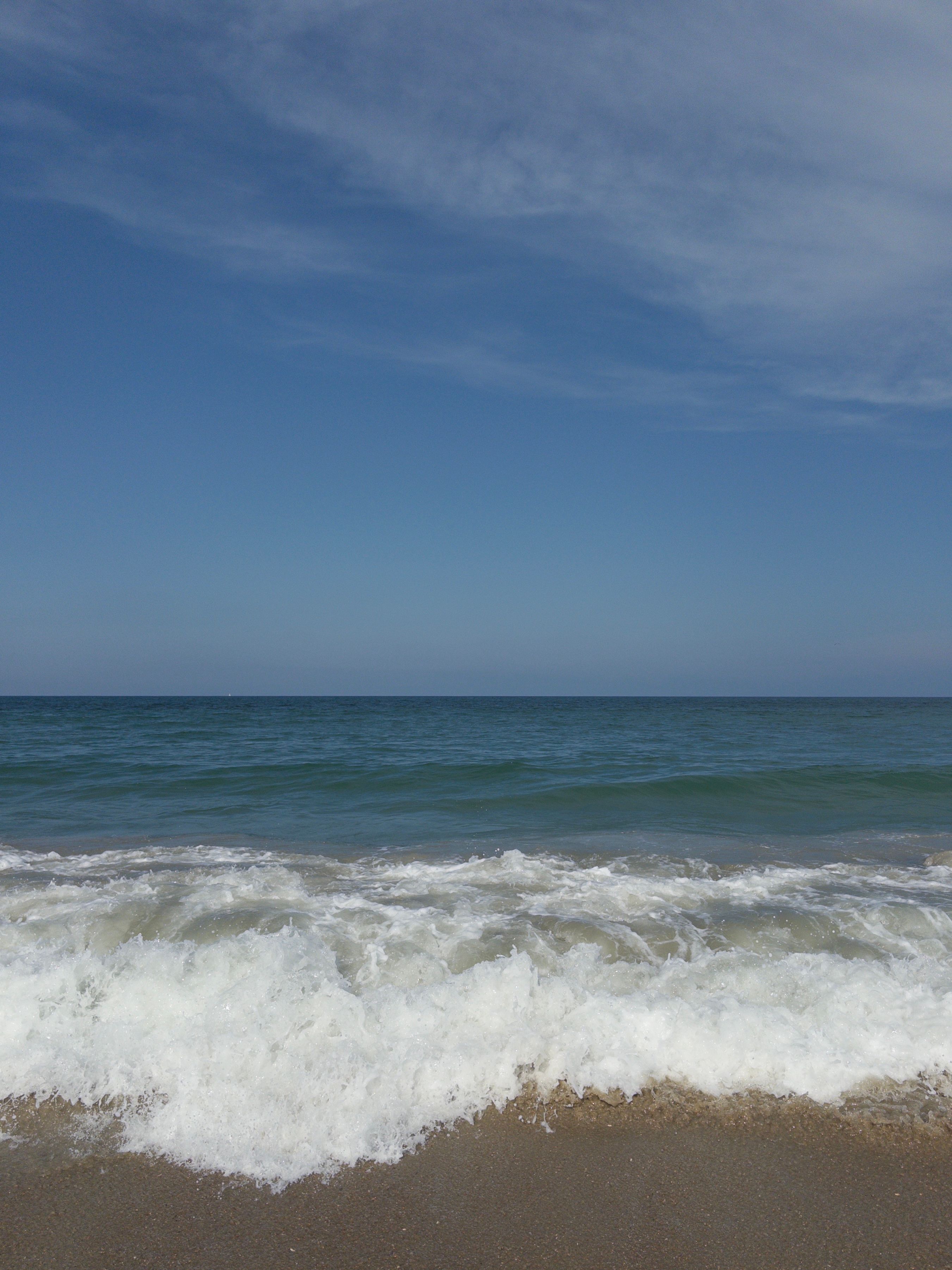 Breaking wave and photographer’s shadow on wet sand, bright blue sky