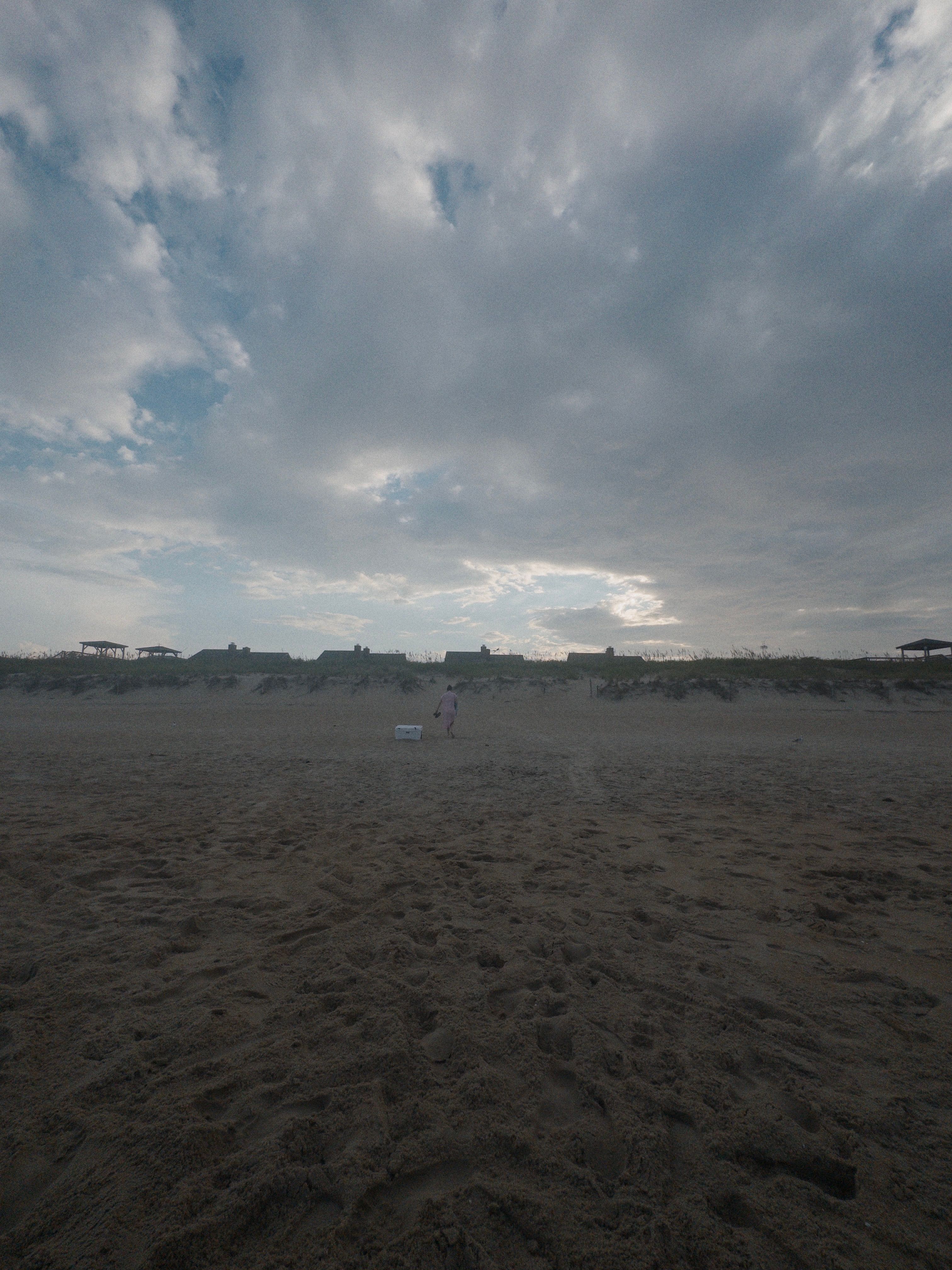 Dunes, a person and a white cooler under an overcast sky